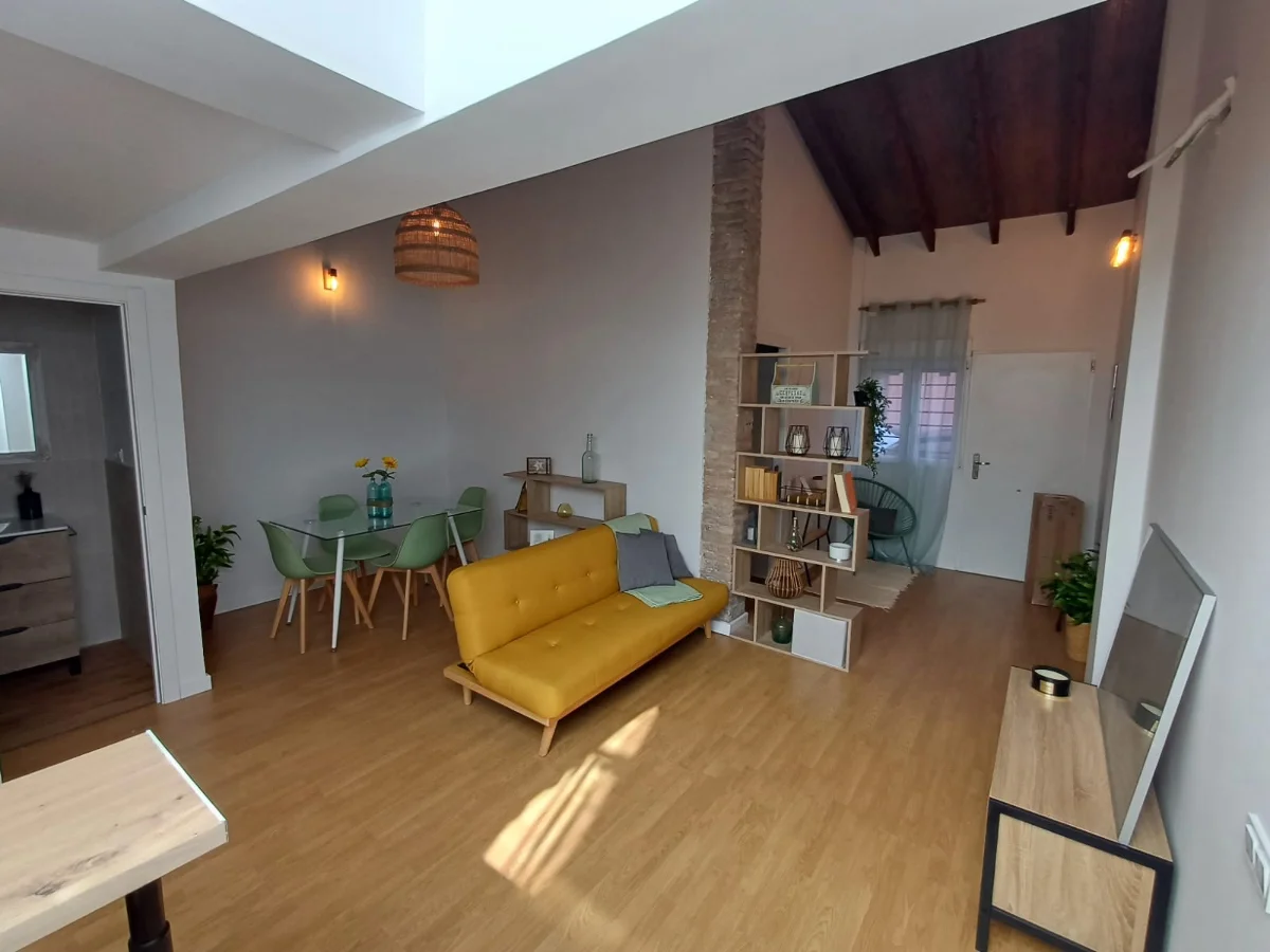 Salón comedor de un adosado reformado, con techo de vigas de madera, suelo de tarima y muro de ladrillo visto.