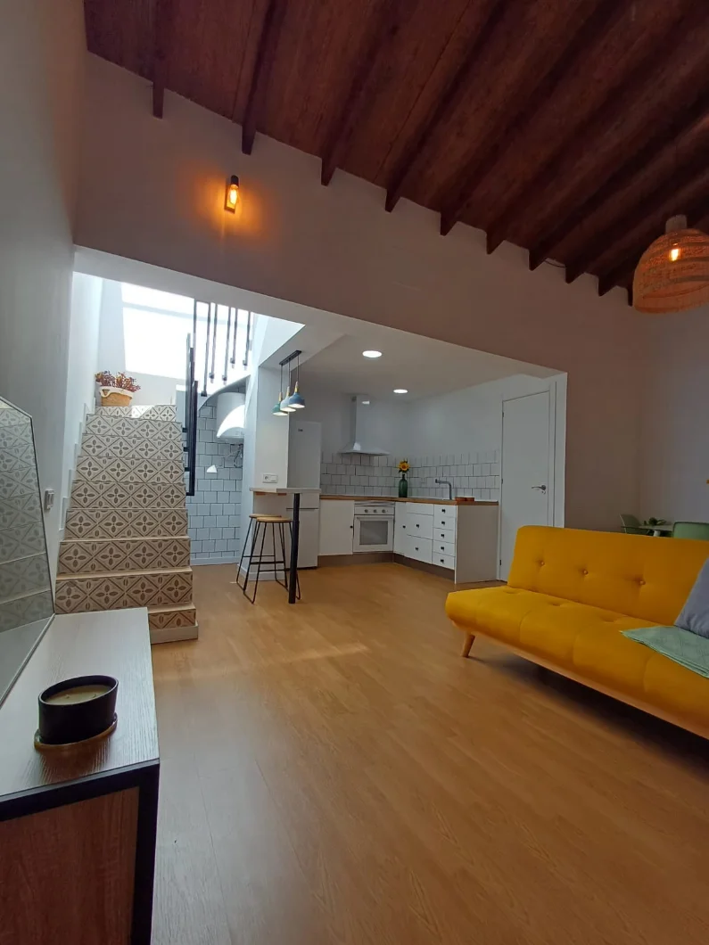 Interior reformado con cocina abierta al salón, escalera con peldaños de baldosa hidráulica y techo de vigas.