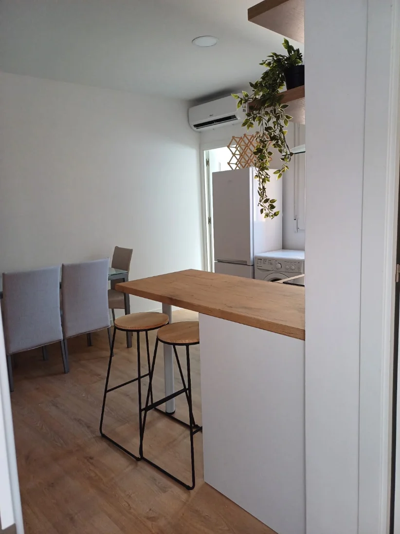 La misma cocina después de la reforma: abierta al salón con barra de madera, taburetes y tarima nueva.