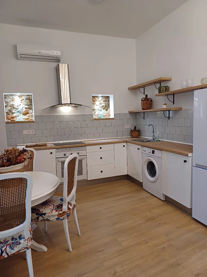 El mismo bajo después de la reforma: cocina blanca con encimera de madera, campana de acero y comedor con mesa redonda.